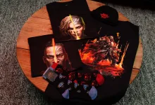 Path of Exile 2 merchandise displayed on a wooden table, including graphic T-shirts, a hat, socks and small accessories.