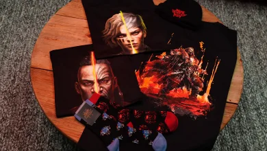 Path of Exile 2 merchandise displayed on a wooden table, including graphic T-shirts, a hat, socks and small accessories.