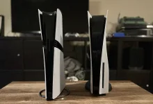 Two white PlayStation 5 consoles stand upright on a wooden table.