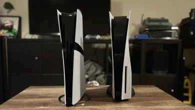 Two white PlayStation 5 consoles stand upright on a wooden table.
