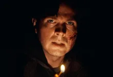 A bloodied young man stares forward by candlelight in a dark scene from the Resident Evil 7 fan film.