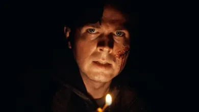 A bloodied young man stares forward by candlelight in a dark scene from the Resident Evil 7 fan film.