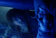 A man looks through wet glass in a dark blue-lit horror scene.