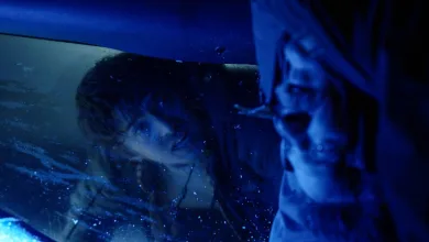 A man looks through wet glass in a dark blue-lit horror scene.