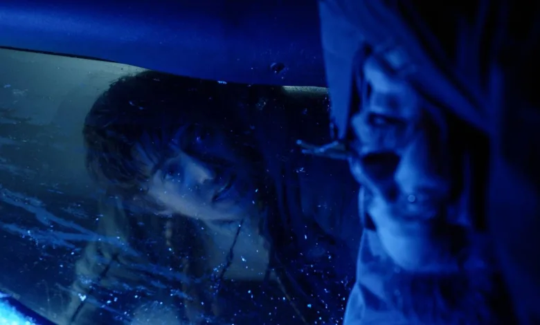 A man looks through wet glass in a dark blue-lit horror scene.