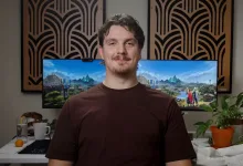 A man sits in front of a monitor displaying RuneScape scenery.