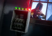 A Rust player stands beside an open heavy fuse box with indicator lights in an industrial room.