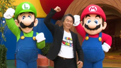 Shigeru Miyamoto poses between Mario and Luigi at Super Nintendo World.