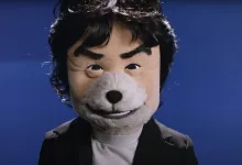 Shigeru Miyamoto wearing a gray furry muzzle against a blue backdrop.