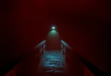 A narrow walkway disappears through red fog toward a dimly lit doorway.