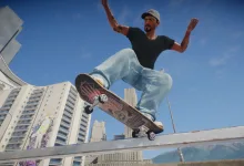 A skate. skater in a black shirt and light jeans performs a skateboard trick above a ledge against a blue sky.