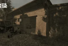 A weathered wooden barn with an open door stands beside an old vehicle in overgrown surroundings.