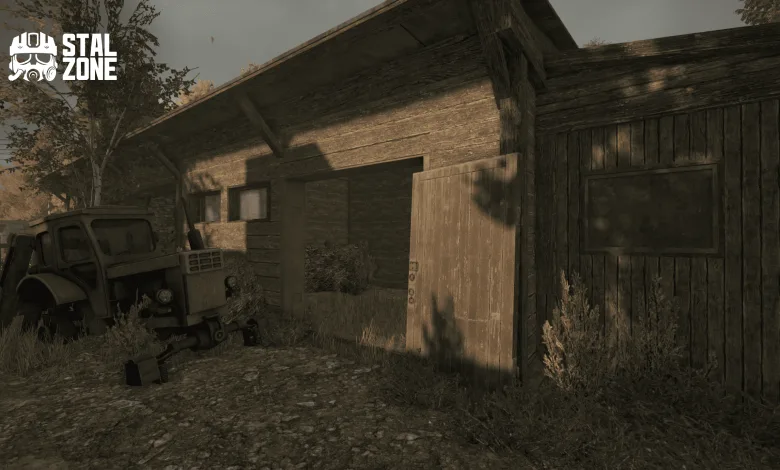 A weathered wooden barn with an open door stands beside an old vehicle in overgrown surroundings.
