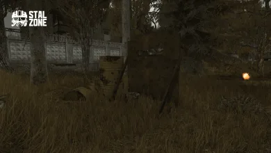 An overgrown area beside a concrete fence, with a barrel, debris, and a small orange glow.