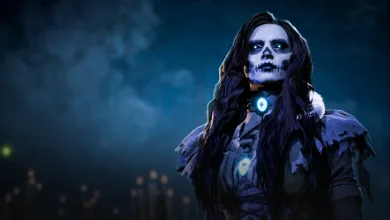 A dark-haired contestant with skull-like makeup and a glowing blue pendant stands against a smoky blue background.