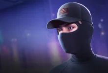 A contestant wearing a dark cap and face covering with an orange emblem against a blue-lit background.