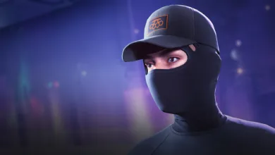 A contestant wearing a dark cap and face covering with an orange emblem against a blue-lit background.
