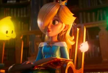 Rosalina sits in a library holding an open book, with yellow and green Lumas nearby.