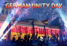 German Unity Day celebration scene with German flags, fireworks, a crowd, and a brightly lit historic building