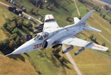 A Q-5D attack aircraft flies over a rural landscape carrying weapons beneath its wings.
