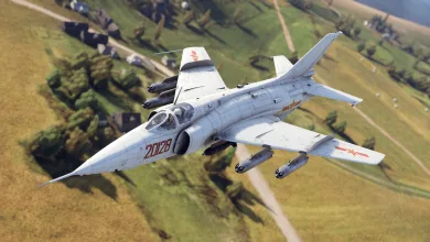 A Q-5D attack aircraft flies over a rural landscape carrying weapons beneath its wings.