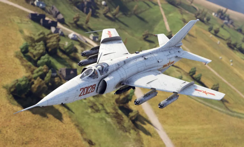 A Q-5D attack aircraft flies over a rural landscape carrying weapons beneath its wings.