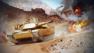 A tan tank drives across rocky desert terrain as smoke and flames rise nearby.