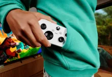 A person tucks a white XBOX Nano Controller into the pocket of a teal hoodie.