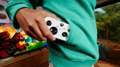 A person tucks a white XBOX Nano Controller into the pocket of a teal hoodie.