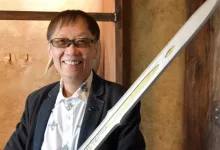 Yuji Horii wearing glasses and a dark jacket beside a sword.