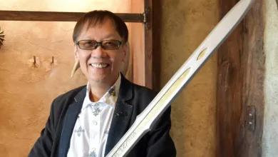 Yuji Horii wearing glasses and a dark jacket beside a sword.